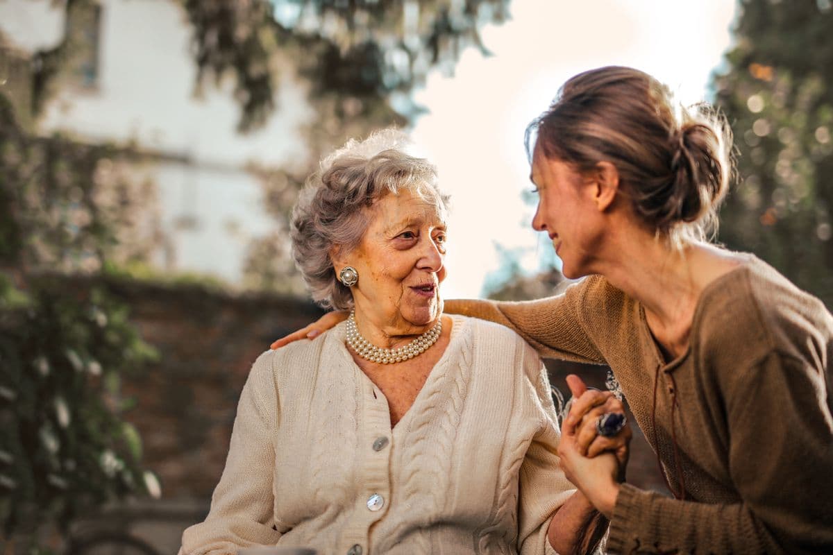 A support worker sharing a warm, unhurried moment with the person she supports in a sunlit garden